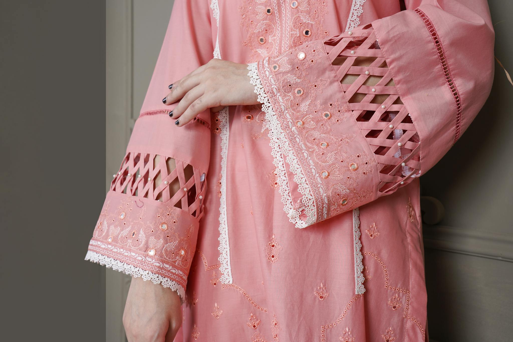 Detailed close-up of a pink embroidered Pakistani dress showcasing intricate lace patterns.