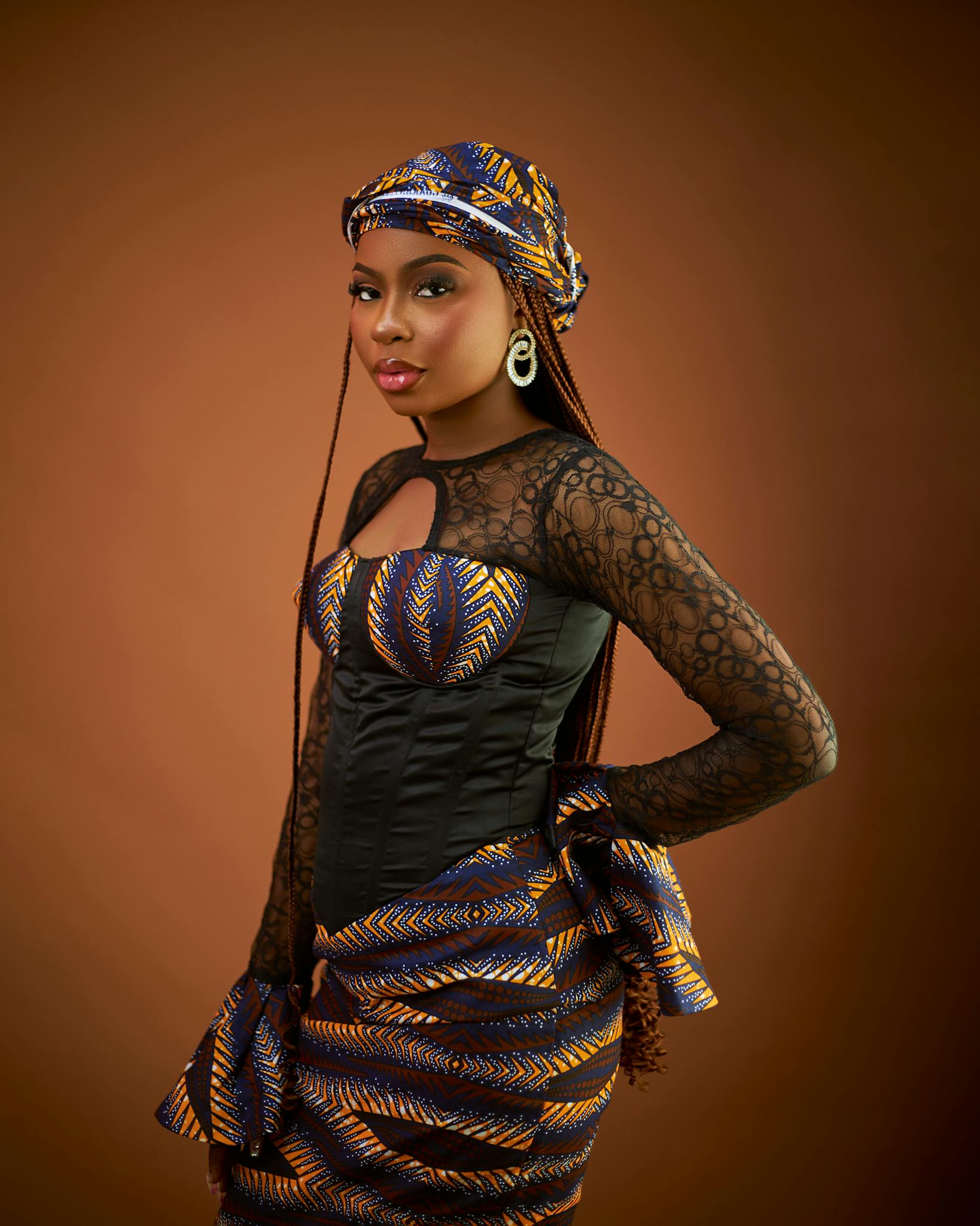 Portrait of a woman in vibrant traditional African dress against a brown background.