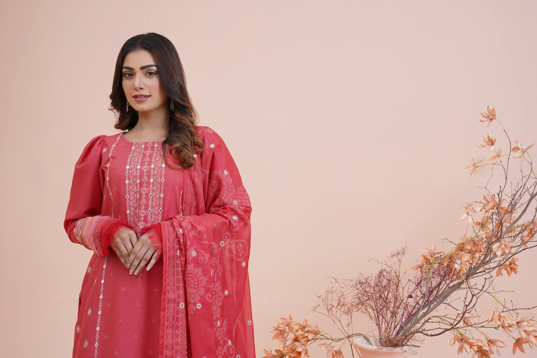 Woman in red traditional Pakistani dress with floral decor, Lahore studio setting.