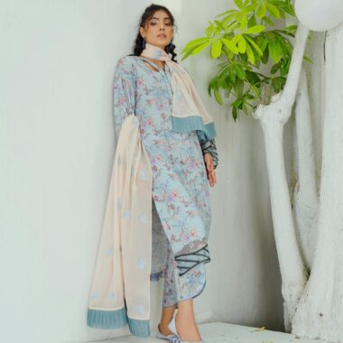 A woman in a traditional floral gown and scarf standing indoors with minimalistic white backdrop