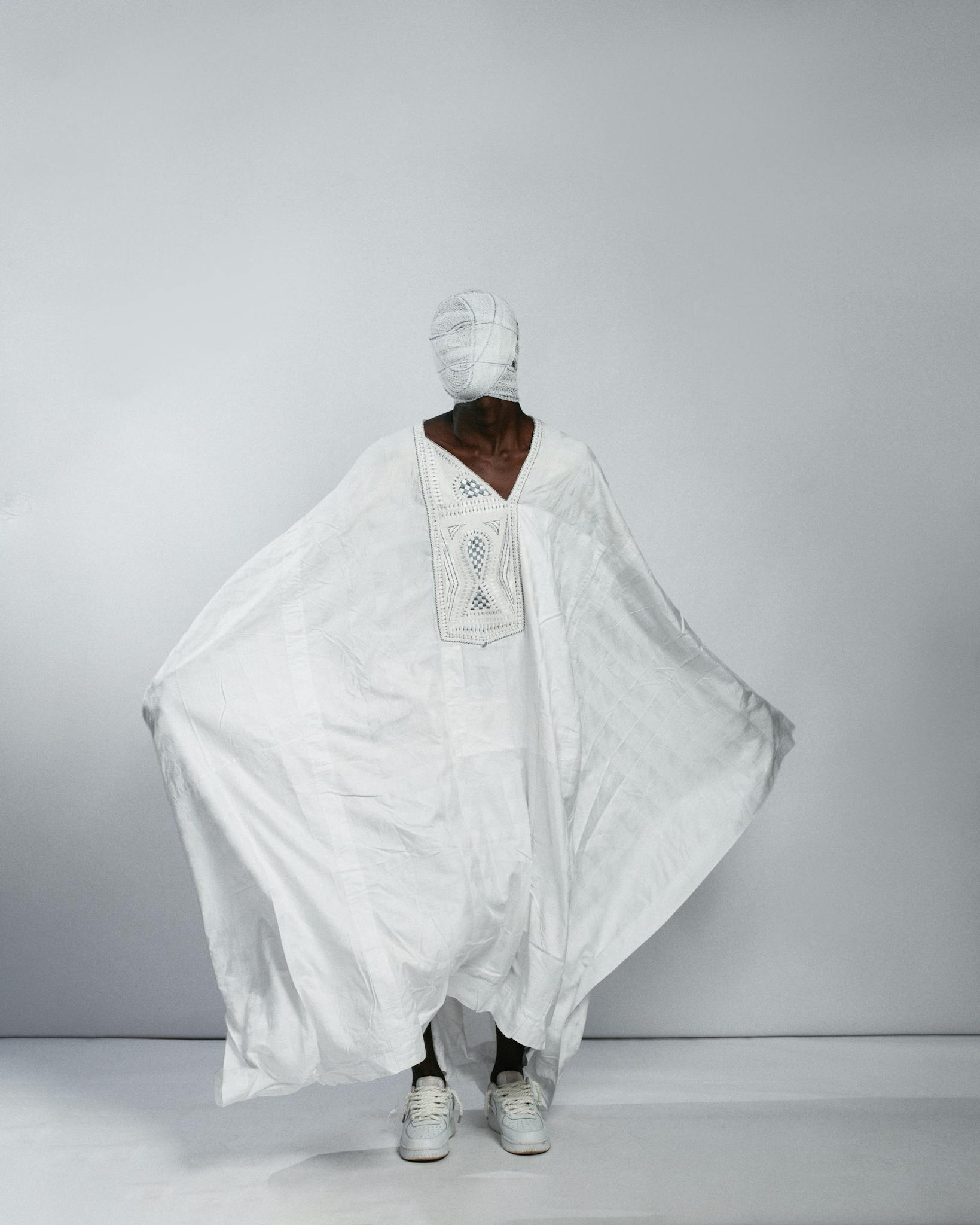 Person draped in white garment, blending modern and traditional styles in a minimalist setting.