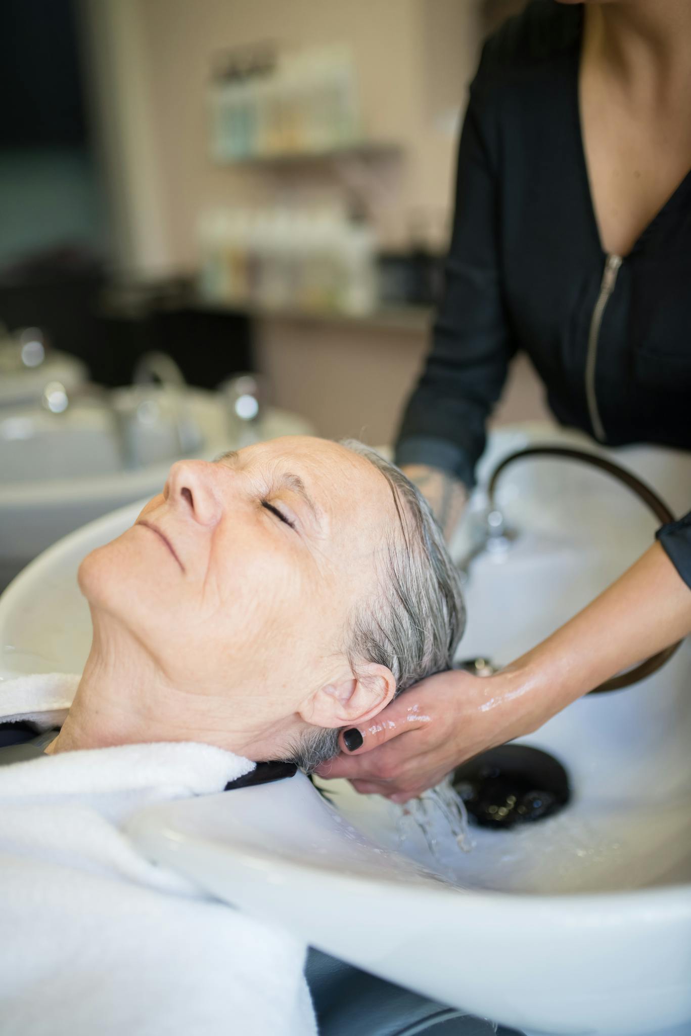 Senior woman enjoying a relaxing hair wash at a salon, emphasizing comfort and care.