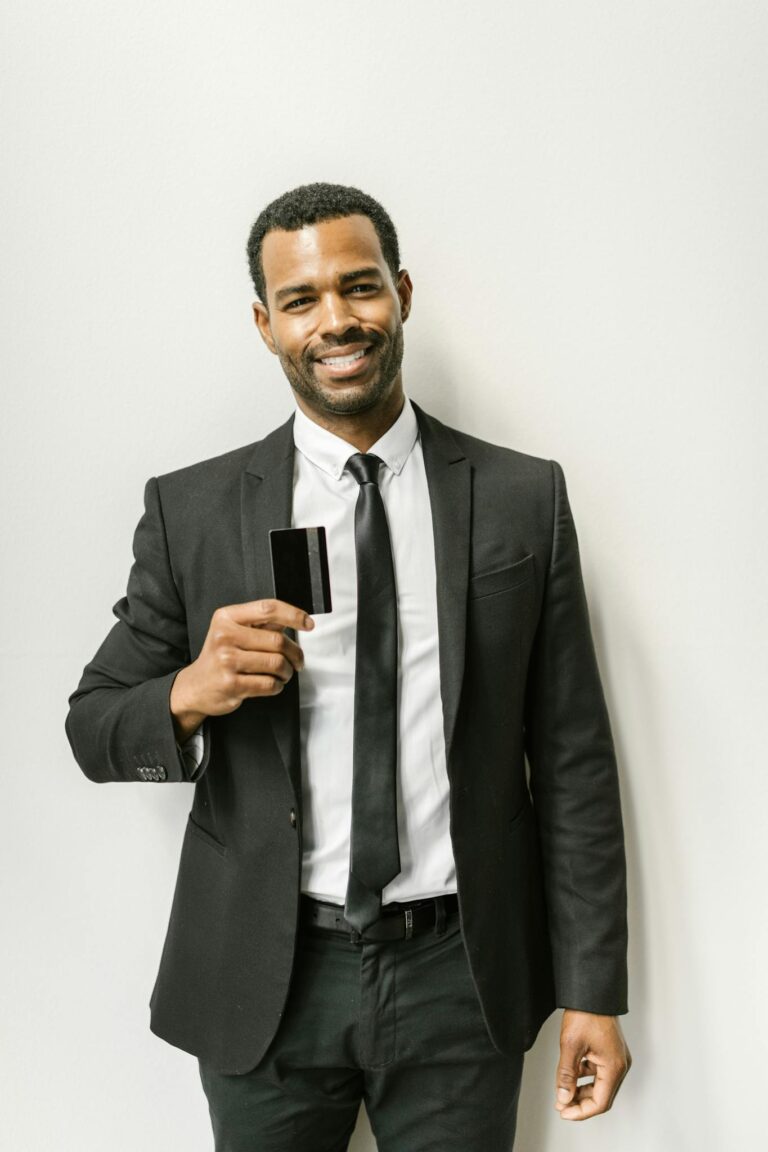 Smiling man in a black suit holding a credit card, symbolizing corporate finance.
